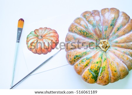 Pumpkin image watercolor painting. Pumpkin vegetable and artwork flat lay composition on table. White work desk with watercolor paintings and brushes. Artist workplace with art supplies and pumpkin
