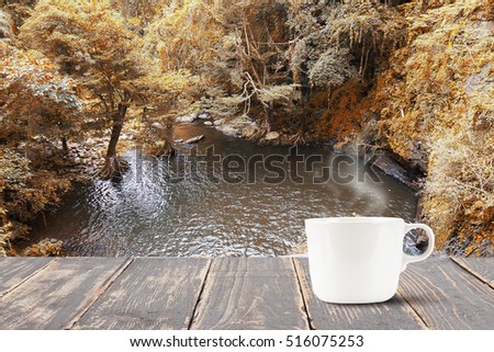 Hot coffee with smoke on vintage wooden table top on blurred waterfall background