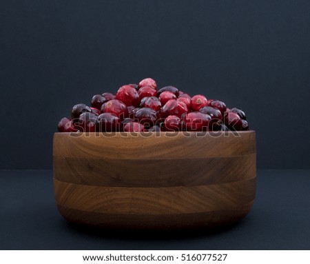 Fresh red and maroon cranberries heaped in a turned wood bowl against a black  background. Photographed at eye level with fill flash and a shallow depth of field.