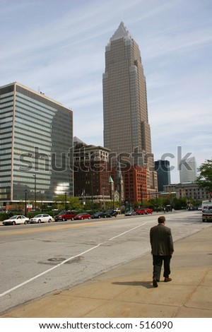 A man walking down a street with the Cleveland Ohio skyline.