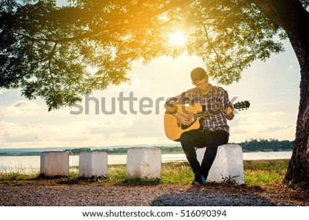 confident man playing the guitar in the air. with sunset on background and blue sky