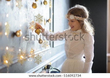 Christmas holidays. Elegantly dressed girl of 8-9 years with delight touches gold Christmas garlands and ornaments. They shine a magic light. Christmas- mysterious and wonderful time. Merry Christmas