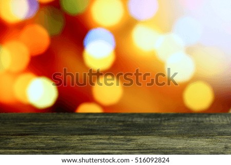 Christmas background with empty old dark wooden desk table. Red, orange, yellow holiday bokeh lights.  Selective focus on wood  foreground and ready for product montage. White copyspace on top corner.