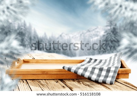 Table of wooden top and free space for your decoration of text or product. Landscape of mountains at winter time. Blurred branches of spruce and frost. 