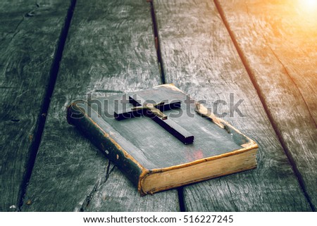 Closeup of wooden Christian cross on bible on the old table. Church utensils.