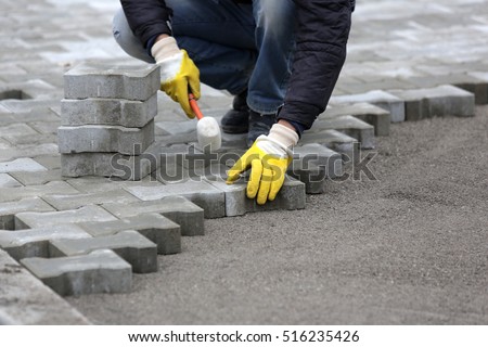 Paving stone worker is putting down pavers during a construction of a city street. Royalty-Free Stock Photo #516235426