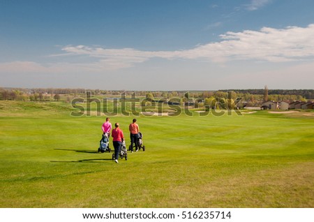 Three women golf players walking on a golf course to the next hole with wheel bags. Sport playground for golf concept - wide landscape as background for your lettering about golf playing. Royal sport.
