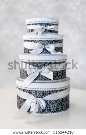 Round celebration gift boxes with silver ribbon bows on white table. Stack of presents in luxury interior