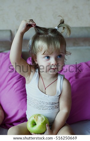 little girl sitting on the couch, biting green apple and takes a bow with hair