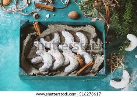 Homemade Christmas nuts cookies crescent with sugar powder in wooden box with holiday star decoration and fir tree over turquoise wood texture surface with copy space. Top view. 