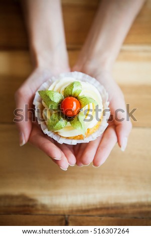 Cupcakes with butter cream and vanilla with physalis on the hands on wooden background