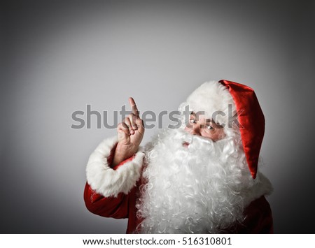 Santa Claus is pointing at something interesting on grey background.
