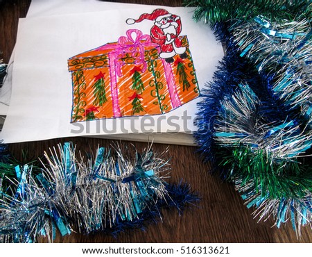 Child's drawing of Santa Claus with a gift. Holiday decorations around the drawing.