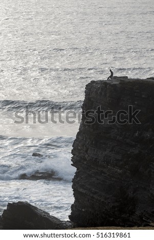 Coastline view of a lonely man on top of cliff gazing the ocean.