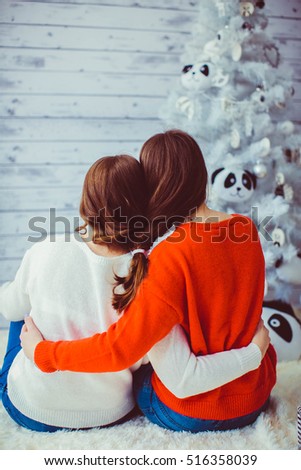 Two cute sisters sitting near the Christmas tree together
