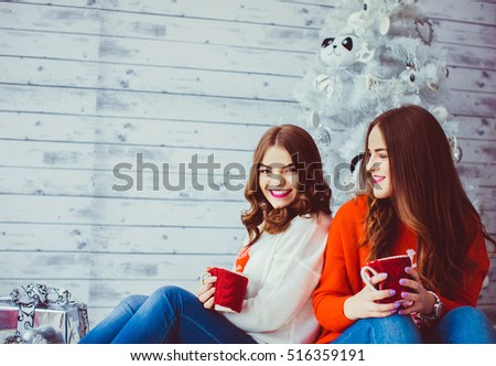 Two happy and beautiful sisters sitting near the Christmas tree