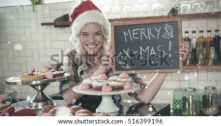 Portrait of woman holding blackboard with merry christmas against snow falling