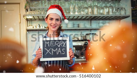 Portrait of happy barista holding Christmas at cafe against snow falling