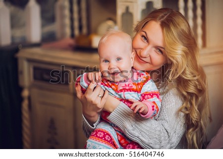 You are my treasure! Side view of cheerful beautiful young woman holding baby girl in her hands and looking at her with love while sitting on the couch at home