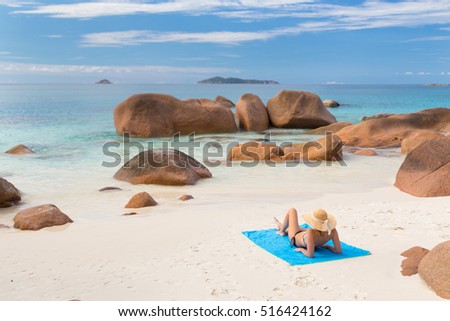 Woman wearing black bikini and beach hat, sunbathing at Anse Lazio beach on Praslin Island, Seychelles. Summer vacations on picture perfect tropical beach concept.