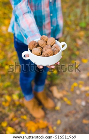 Girl holding a bowl of walnuts standing in the autumn forest. Soft focus.