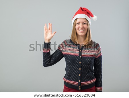 Pretty woman wearing Santa hat showing Vulcan greeting isolated on gray