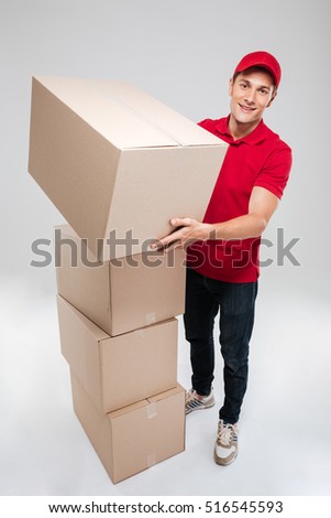Full length of young delivery man near the boxes. isolated gray background