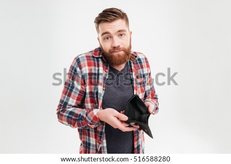 Upset young bearded man in plaid shirt holding empty wallet over white background Royalty-Free Stock Photo #516588280