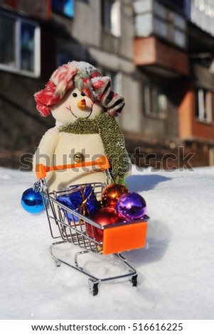 Snowman with a small supermarket trolley and gifts in snow