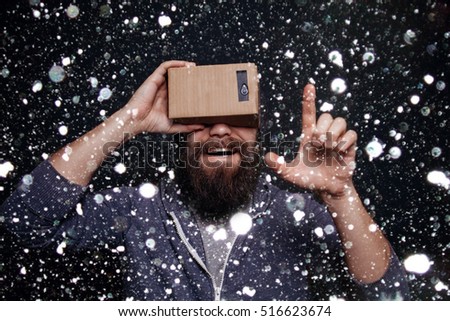 Color shot of a young man looking through a card board, a device with which one can experience virtual reality on a mobile phone. winter .over snow background
