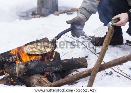 view background people bake pancakes on a fire in the open air in the winter on a holiday Maslenitsa