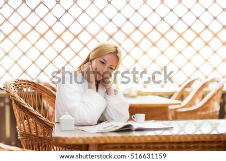 Beautiful girl drinking coffee. A young woman sits in a beautiful sunny place with a cup of coffee and reading a magazine.