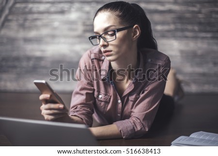 Attractive young female lying on wooden floor, using laptop and cellphone. Leisure time concept