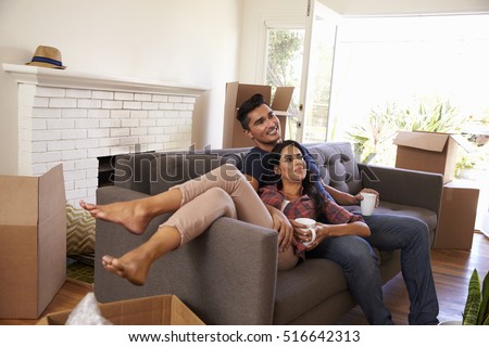 Couple On Sofa Taking A Break From Unpacking Watching TV Royalty-Free Stock Photo #516642313
