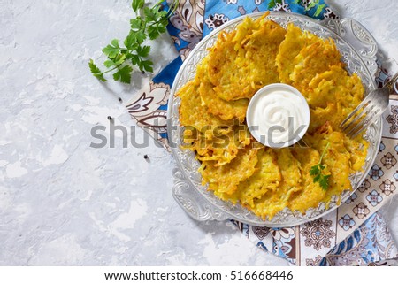 Homemade traditional potato pancakes, served with sour cream sauce, top view. Hanukkah holiday meal on vintage concrete background. Copy space.