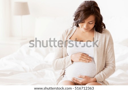 pregnancy, rest, people and expectation concept - happy pregnant woman sitting on bed and touching her belly at home Royalty-Free Stock Photo #516712363
