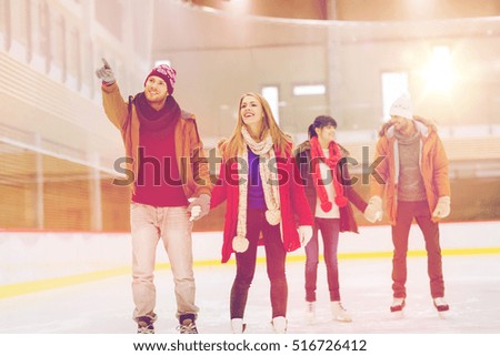 people, friendship, sport, gesture and leisure concept - happy friends pointing finger on skating rink