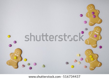 Hand decorated gingerbread men on a pastel grey background with candy and blank space in middle
