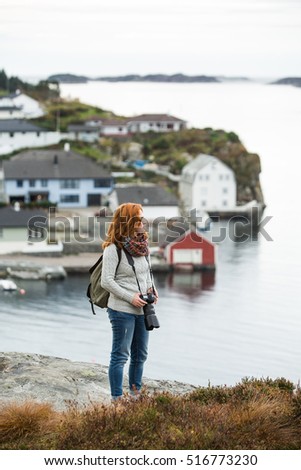 Red-haired girl with glasses standing on top of a hill on a background of ocean and islands. Overcast. Scandinavia.