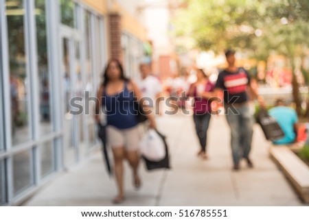 Blurred image of people out shopping at pedestrian outdoor courtyards and covered walkways in outlet mall in Houston, Texas, US. Wide range of retailers of designer apparel, jewelry, fine leather.