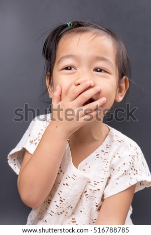 close up photo of a cute little asian girl wearing a white shirt Hands off at the mouth on a gray background.