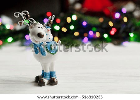 christmas reindeer toy on background of colorful garland lights. stylish rustic white wooden table. space for text. holiday greeting card concept