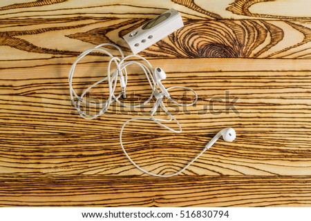 Old white mp3 flash player and white earphones lie on the wooden desktop.