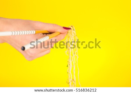 Hand holding chopsticks, eating noodles yellow background