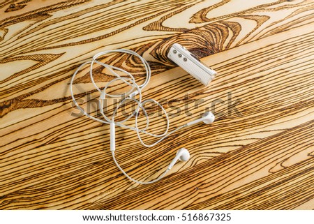 Old white mp3 flash player and white earphones lie on the wooden desktop.