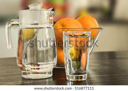 Pitcher and glass of water with bowl of fruits on the background.