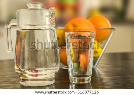 Pitcher and glass of water with bowl of fruits on the background.