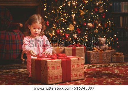child girl in a nightgown in the Christmas night opening gifts at the Christmas tree