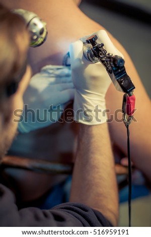 Tattoo master tattooing on young man