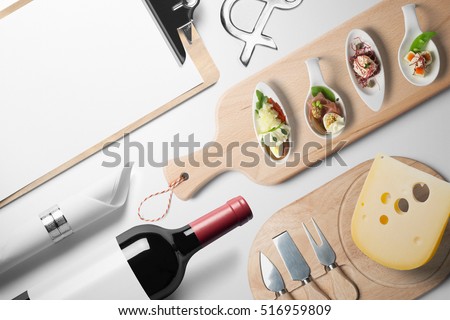 Blank restaurant menu template, on white table with wine bottle canapes and cheese, top view.